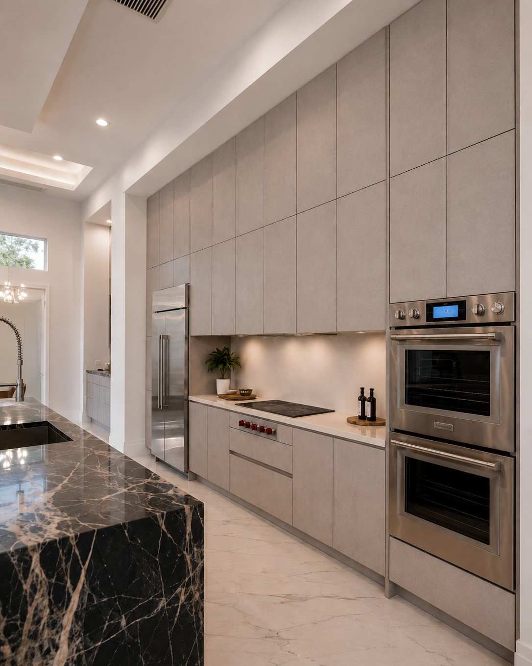 Galley kitchen with floor-to-ceiling matte grey slab cabinetry, stainless double wall oven and integrated refrigerator, and a black marble waterfall island over polished white marble flooring.