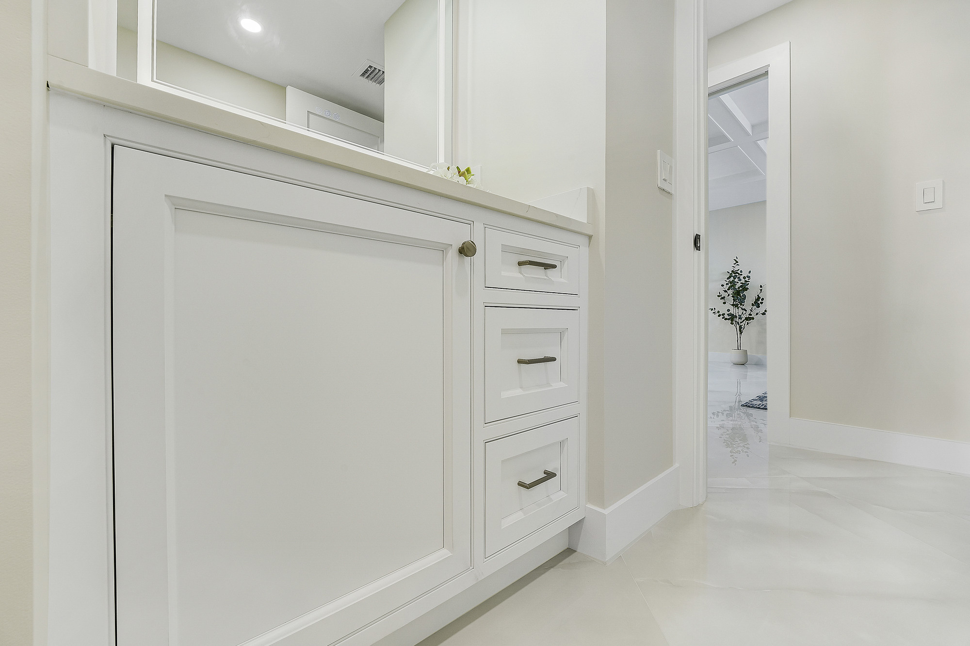 Close view of white inset cabinetry with brushed metal pulls and a quartz top in a hallway, with a doorway leading to a polished marble-look floor.