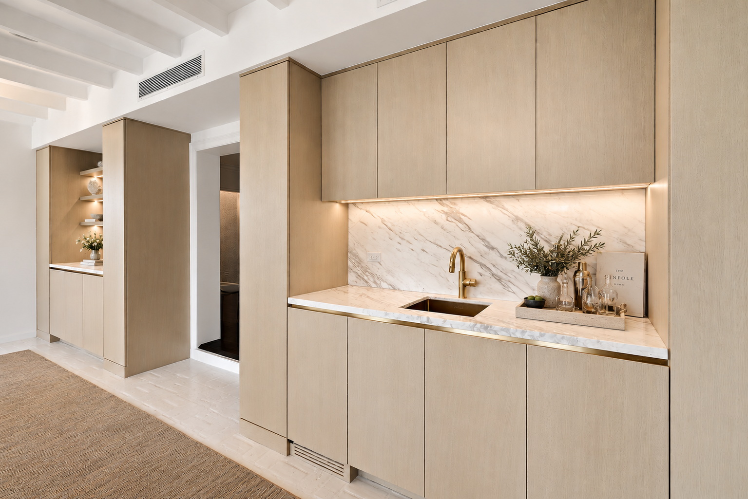 Oak wet bar with a marble backsplash, brass fittings and an undermount sink, with lit display shelving beyond
