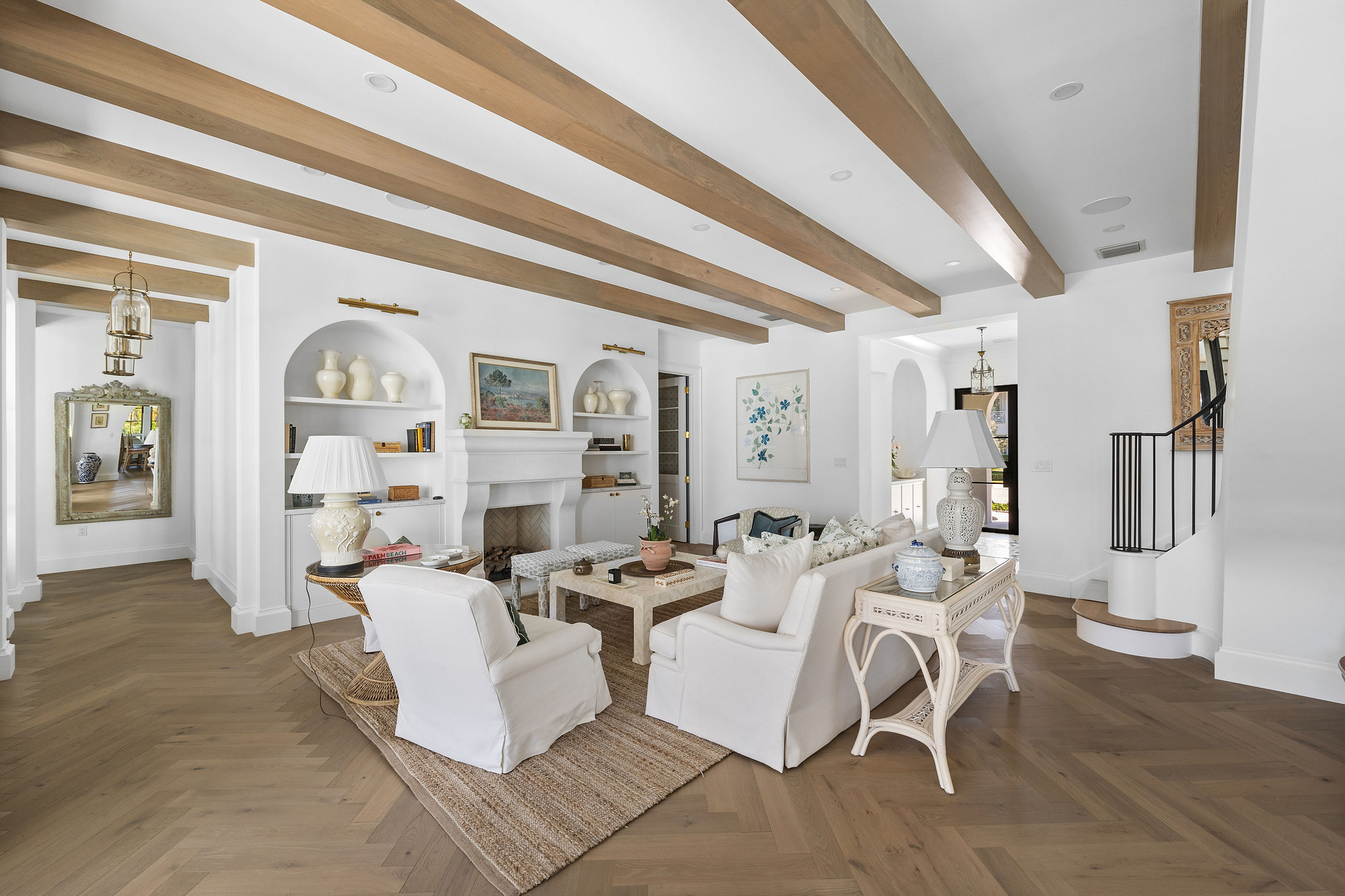 Wide living room with light oak ceiling beams, a cast stone fireplace flanked by arched built-in niches, and herringbone oak flooring.
