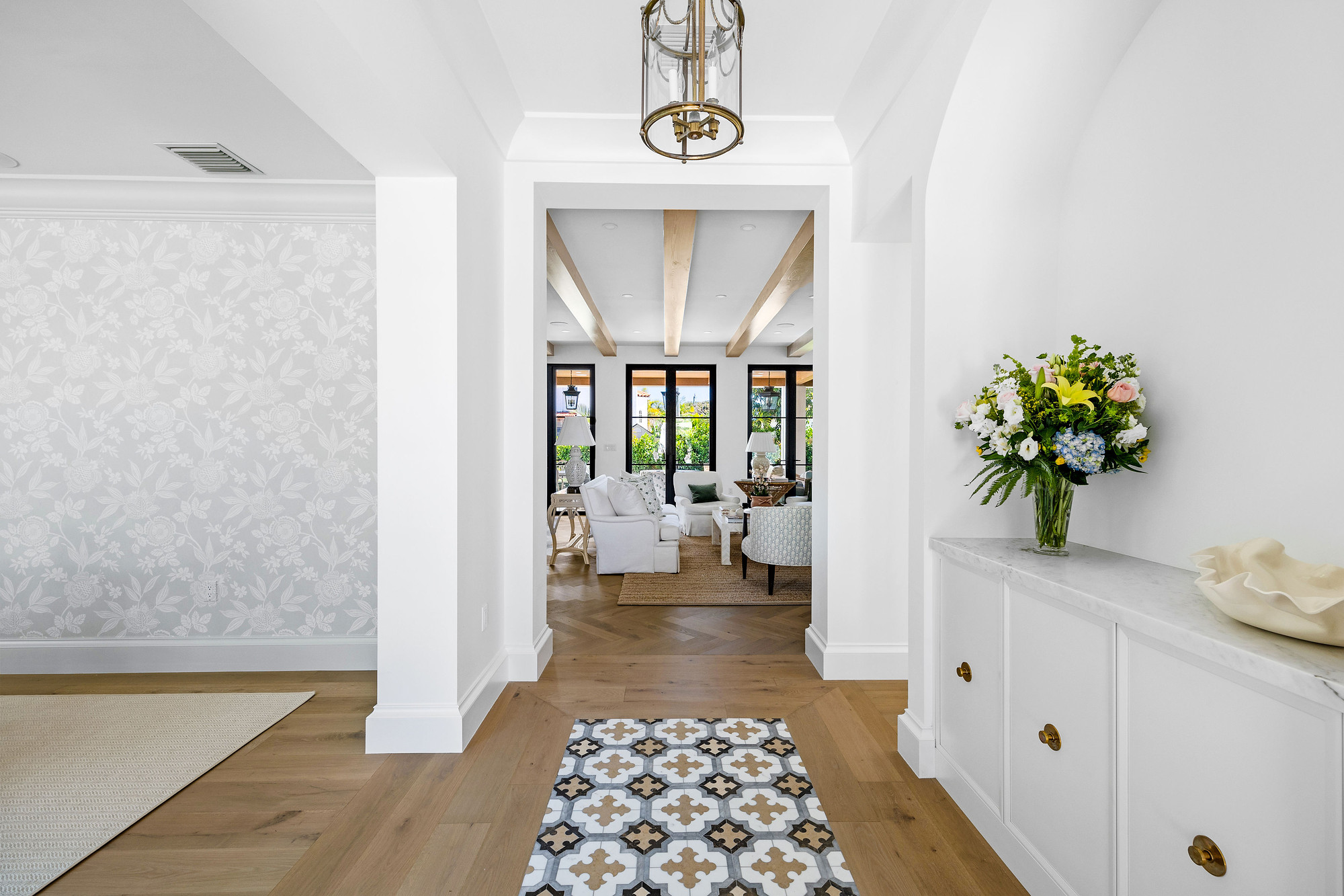 Foyer with floral wallpaper, a patterned tile runner inlaid into oak flooring, arched niche cabinetry with brass knobs and a brass lantern overhead.