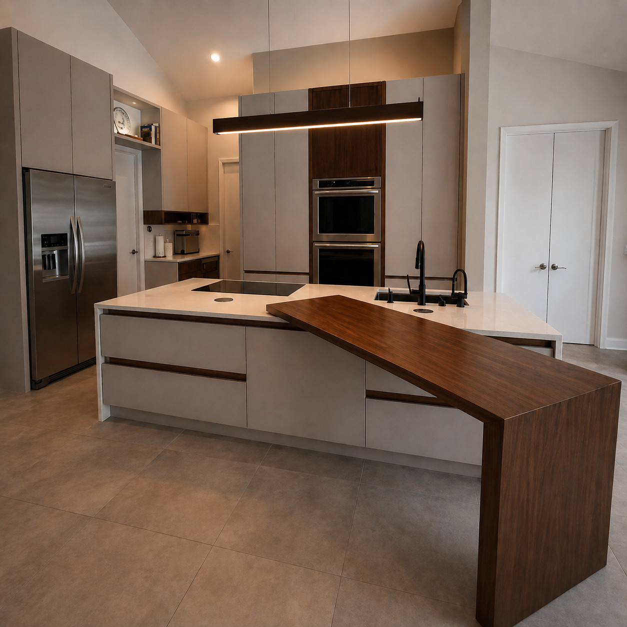 Wide view of a contemporary kitchen with a walnut bar top extending from a white quartz island, handleless greige cabinetry, stainless side-by-side refrigerator and double wall oven, black faucets, a linear pendant and large-format grey floor tile.