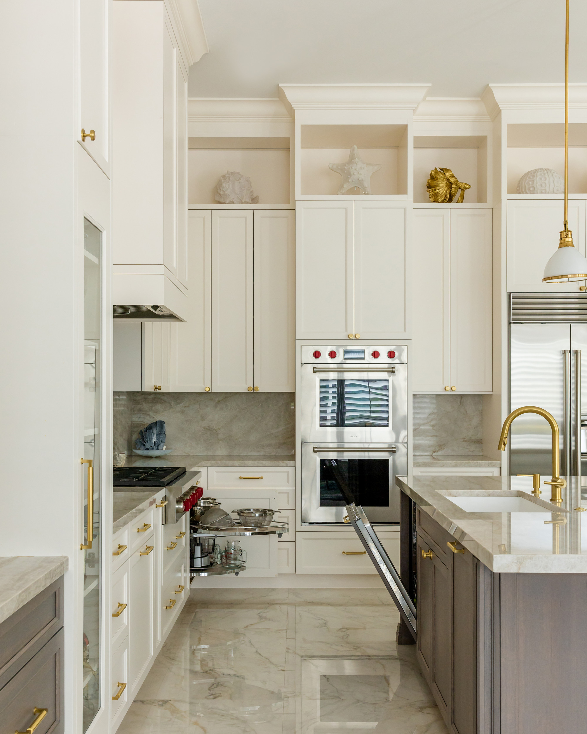 Kitchen interior with ivory cabinetry, stainless double wall ovens, quartzite backsplash and a pull-out corner storage unit with cookware exposed next to an open dishwasher panel.
